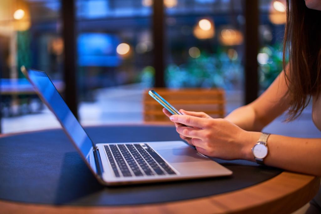 responsive web design concept - woman using a phone and laptop in a cafe